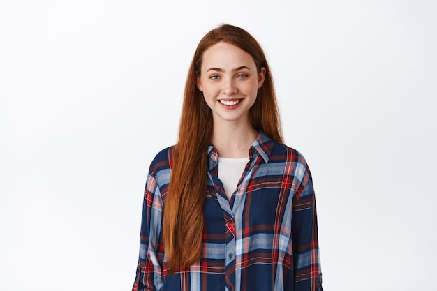 Smiling redhead girl with long hair, pale natural skin no make up, smile white teeth, standing in plaid shirt and looking happy, white background.