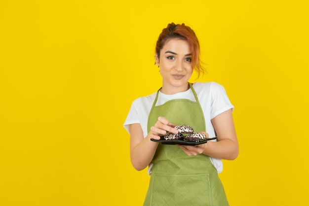 Smiling redhead taking fresh cookie from pile on yellow wall