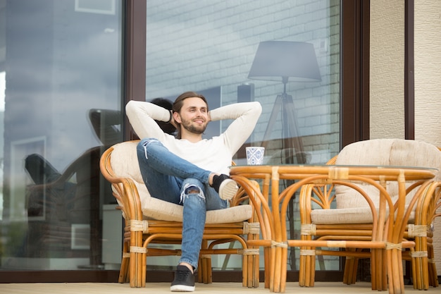 Foto gratuita uomo rilassato sorridente che gode della mattina piacevole che si siede sul terrazzo all'aperto