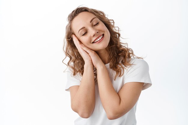 Smiling romantic girl daydreaming remember happy beautiful moment close eyes and imaging something leaning on hands dreamy sleeping standing over white background