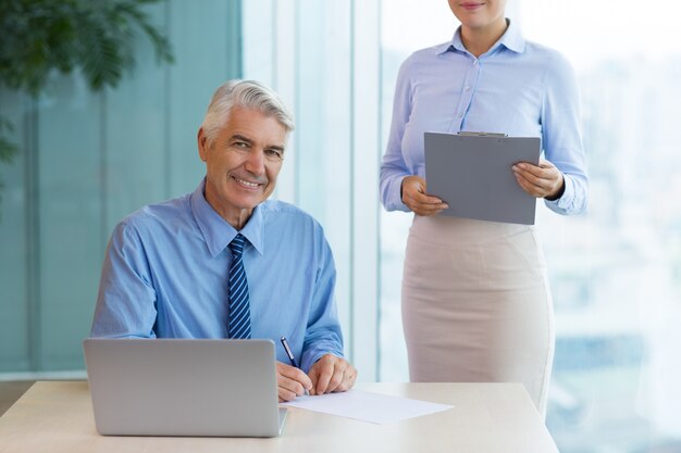 Smiling Senior Boss Signing Document and Secretary