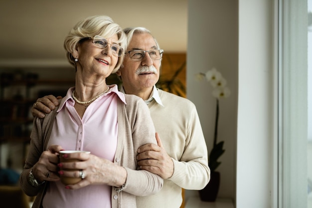 Smiling senior couple standing embraced and looking through the window