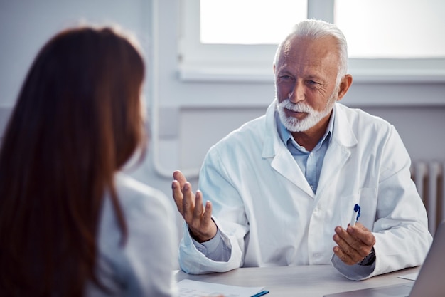 Smiling senior doctor and his female patient communicating during an appointment at doctor's office