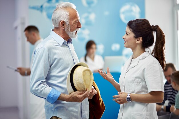 Smiling senior man communicating with a nurse while standing in a lobby at medical clinic