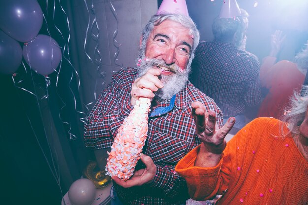 手でシャンパンのボトルを保持している年配の男性と彼女の妻が空気で紙吹雪を投げて笑顔