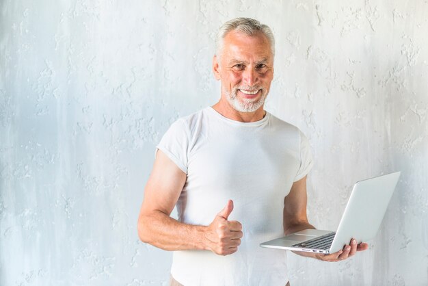 Smiling senior man holding laptop showing thumb up sign