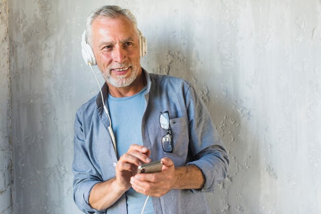 Smiling senior man listening music on headphone through mobile