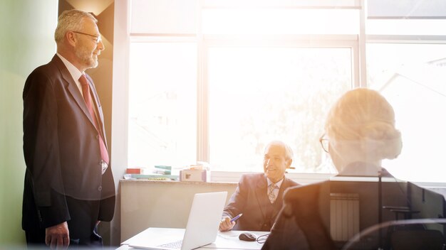 Smiling senior man looking at his coworker working in the office