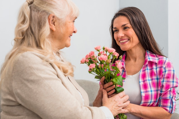 シニアの母親と彼女の娘がバラの花束を持って笑顔