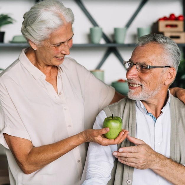 Smiling senior woman giving green apple to her husband