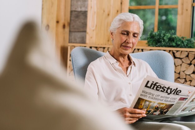 Smiling senior woman reading newspaper at home