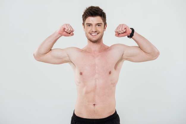 Smiling shirtless sportsman showing biceps and looking at camera