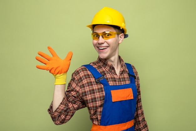 Улыбаясь, показаны пять молодых мужчин-строителей в униформе и перчатках с очками