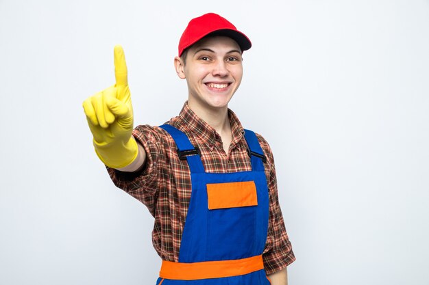 Smiling showing one young cleaning guy wearing uniform and cap with gloves 