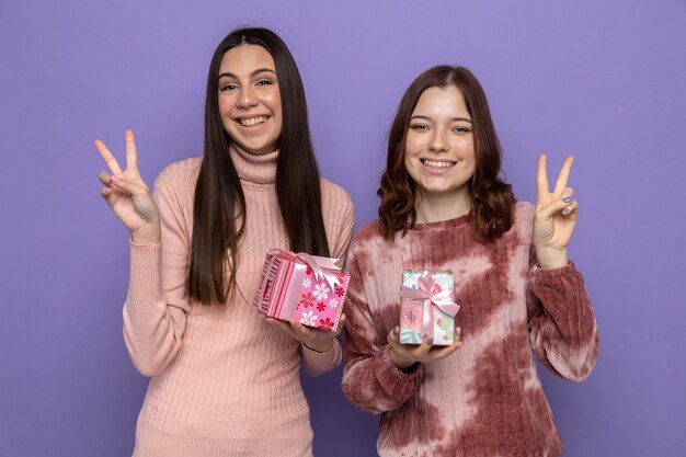 Smiling showing peace gesture two girls holding presents 