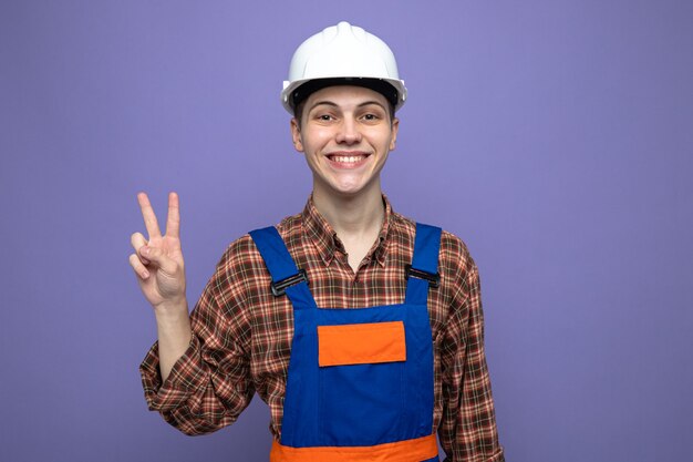 Smiling showing peace gesture young male builder wearing uniform 