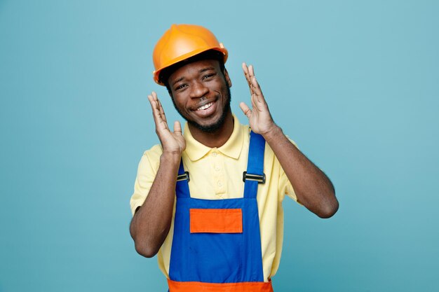 smiling showing size young african american builder in uniform isolated on blue background