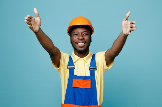 Smiling showing size young african american builder in uniform isolated on blue background