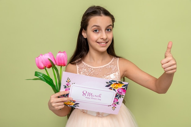 Smiling showing thumb up beautiful little girl on happy women's day holding flowers with greeting card 