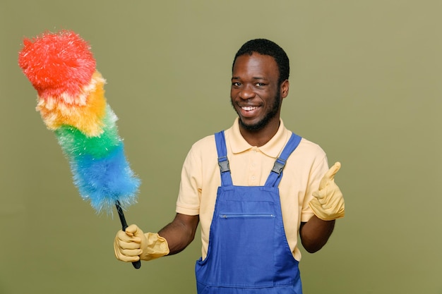 smiling showing thumbs up holding pipidaster young africanamerican cleaner male in uniform with gloves isolated on green background