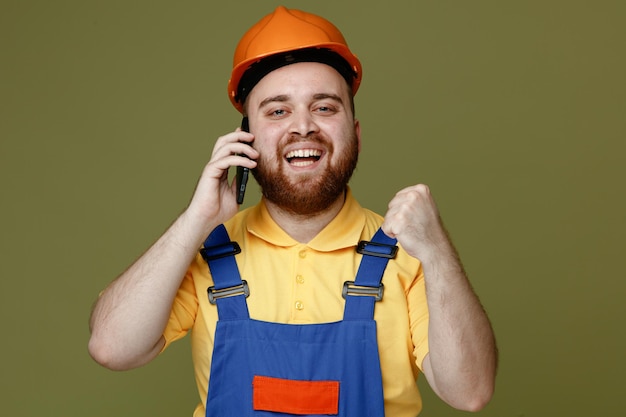 緑の背景に分離された制服を着たはいジェスチャー若いビルダー男を示す笑みを浮かべてください。