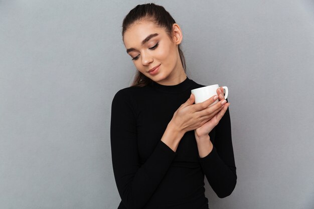 Smiling shy brunette woman in black clothes holding cup of coffee