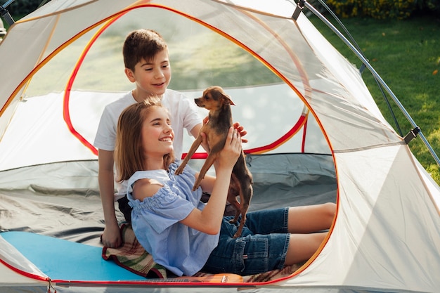 Smiling sibling stroking little dog in tent at picnic