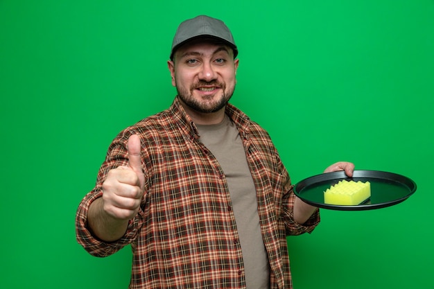 Smiling slavic cleaner man cleaning dishes with sponge and thumbing up 