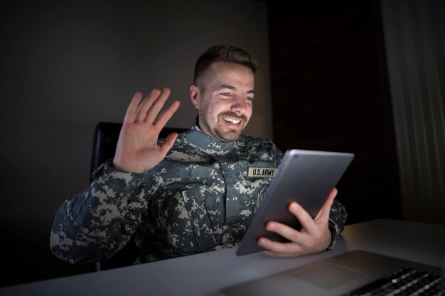 Улыбающийся солдат в военной форме воссоединяется со своей семьей через планшетный компьютер