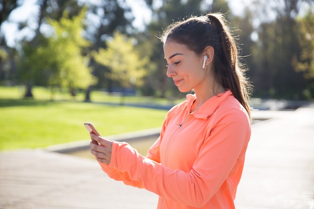 公園でスマートフォンを使用してスポーティな女性の笑みを浮かべてください。