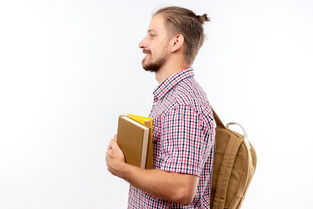 Улыбаясь, стоя в профиль, молодой парень студент носить рюкзак, держа книги