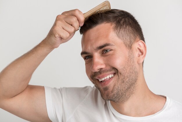 Smiling stubble man comb his hair against white backdrop