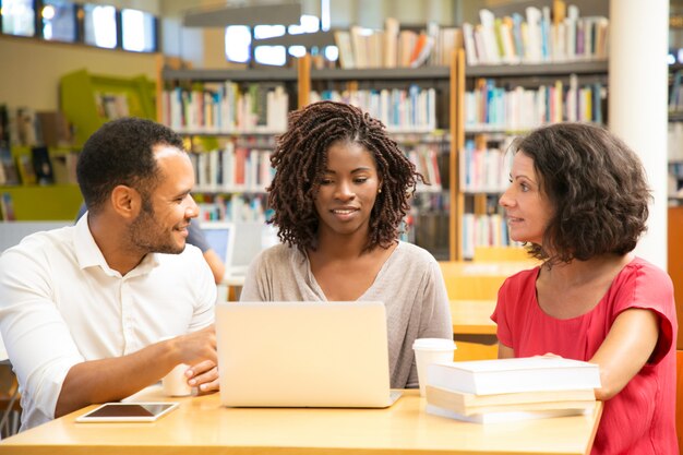 Smiling students discussing something while working with laptop