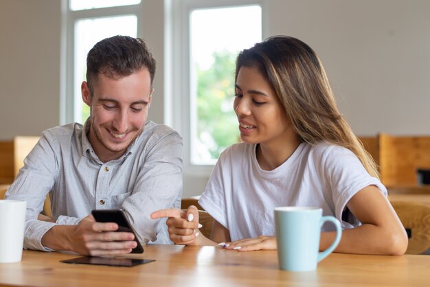 Smiling students drinking tea and using smartphone in cafe