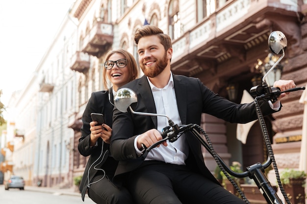 Le coppie alla moda sorridenti guidano sulla motocicletta moderna all'aperto