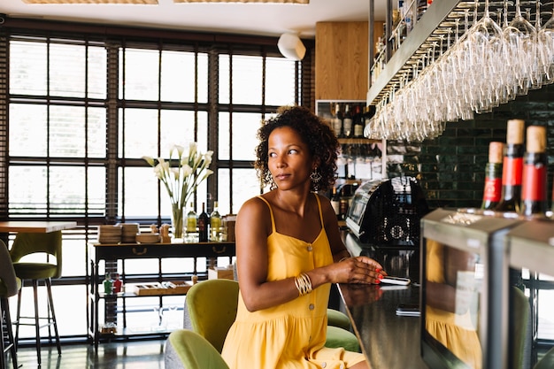 Free photo smiling stylish young woman sitting at bar counter holding smart phone in the restaurant