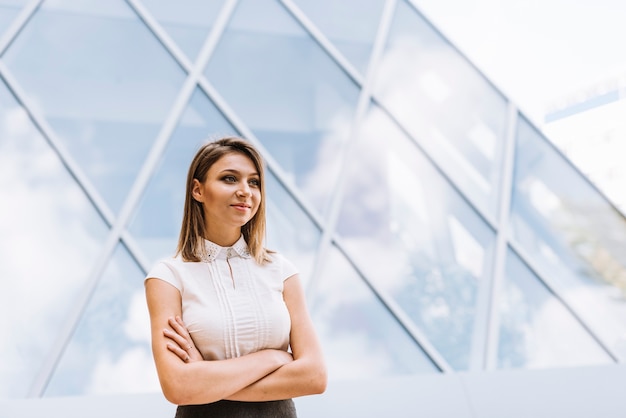 Smiling successful young businesswoman standing in front of modern building