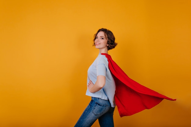 Free photo smiling supergirl in jeans standing in confident pose on yellow space