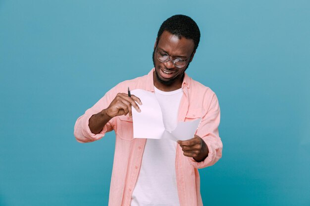 Smiling tears paper young africanamerican guy isolated on blue background