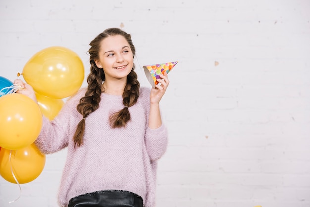 Palloncini sorridente della tenuta dell'adolescente e cappello del partito che distolgono lo sguardo