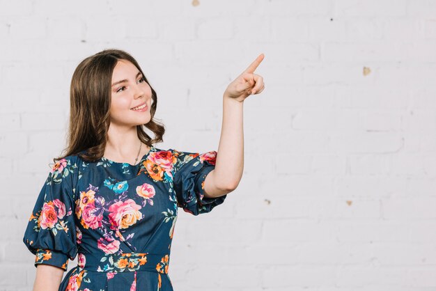 Smiling teenage girl pointing her finger at something against backdrop