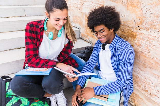 Smiling teenage girl showing something on book to her friend