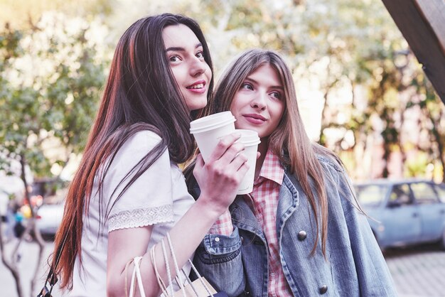 Smiling teenage girls with coffee cups on street. Drinks and friendship concept.