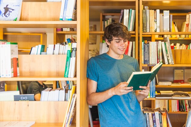 Smiling teenager leaning on bookcase and reading