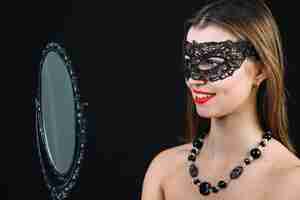 Free photo smiling topless woman in carnival mask looking in hand mirror