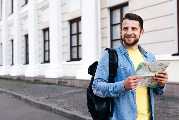 Smiling traveler man holding map looking away standing on street