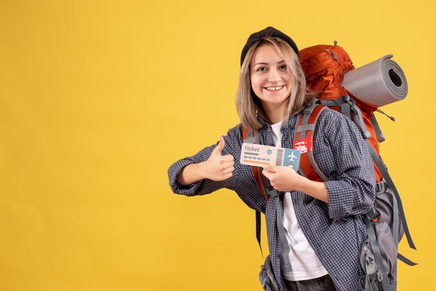 smiling traveler woman with backpack holding ticket giving thumbs up