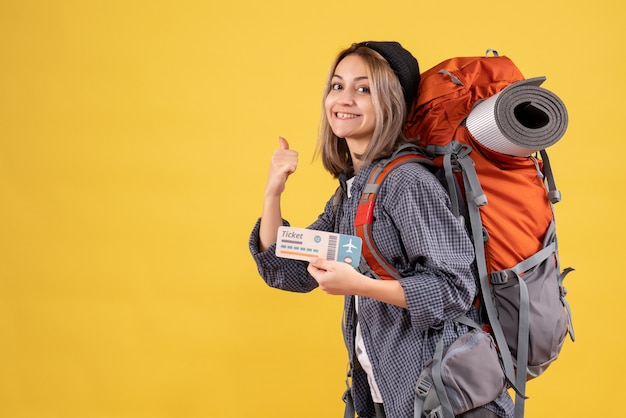 smiling traveler woman with backpack holding ticket pointing finger behind