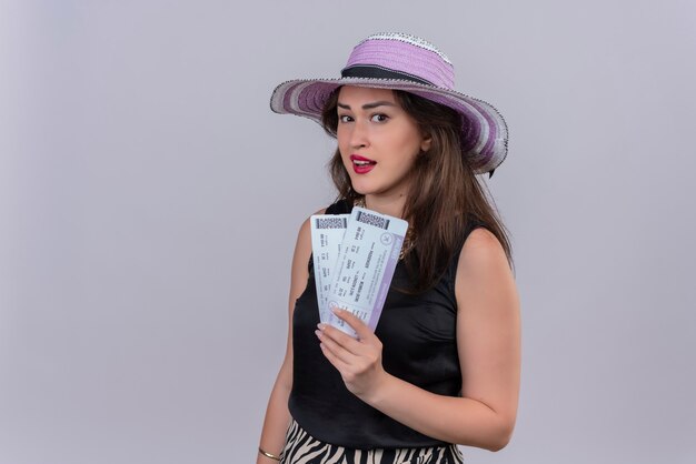 Smiling traveler young girl wearing black undershirt in hat holding tickets on white background