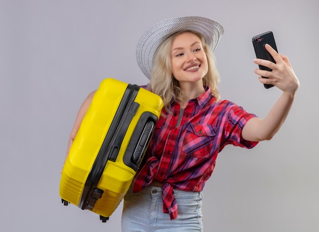 모자 가방을 들고와 격리 된 흰색 배경에 셀카를 복용에 빨간 셔츠를 입고 여행자 어린 소녀 미소